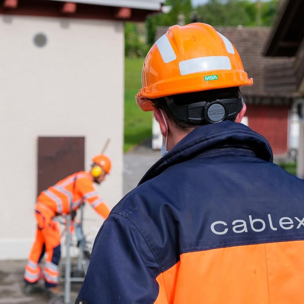Ein cablex-Mitarbeiter von hinten mit cablex-Jacke und orangem Helm
